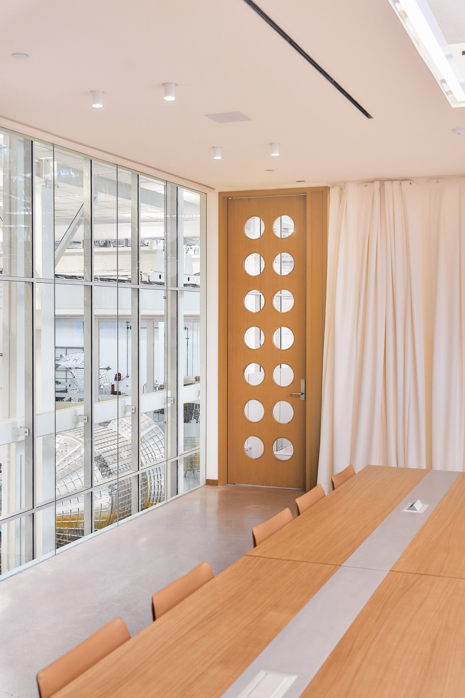 Photo of a mezzanine meeting room at Vast's Long Beach headquarters showing a view onto the fabrication floor through floor-to-ceiling windows